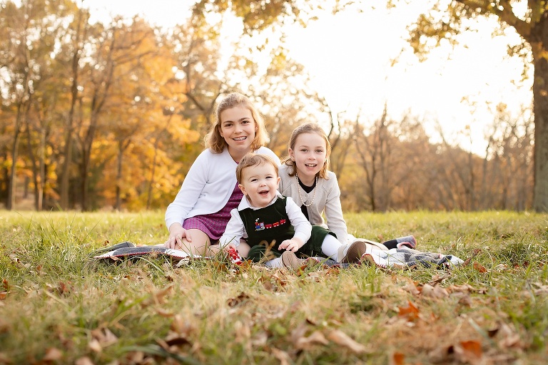 All three siblings sitting on blanket on fall evening smiling at camera | STL Family Photographer
