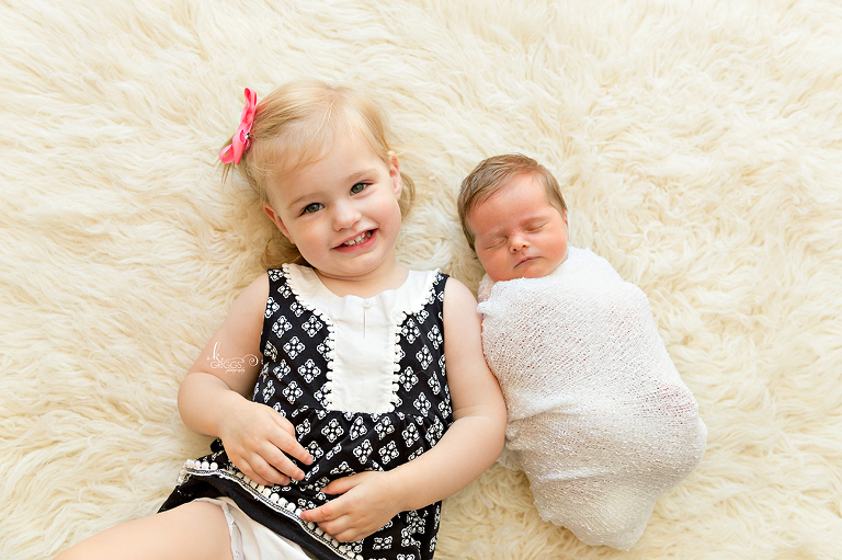 Big sister with baby sister on rug | St. Louis Newborn Photography