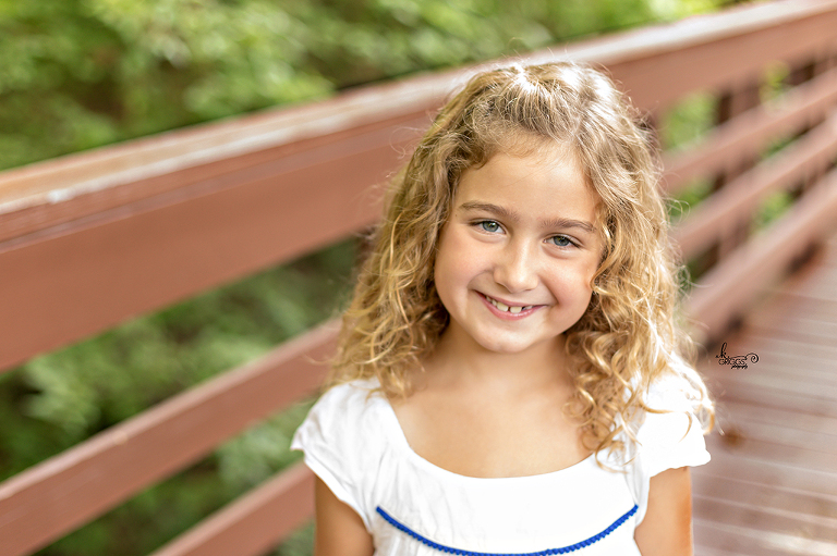 Young girl in white dress on bridge smiling. | St. Louis Family Photographer