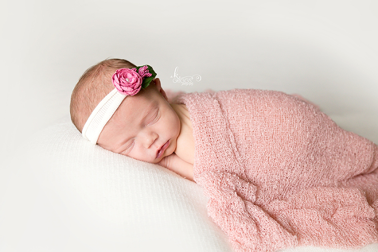 Newborn baby girl with headband and pink wrap. | St. Louis Photographer