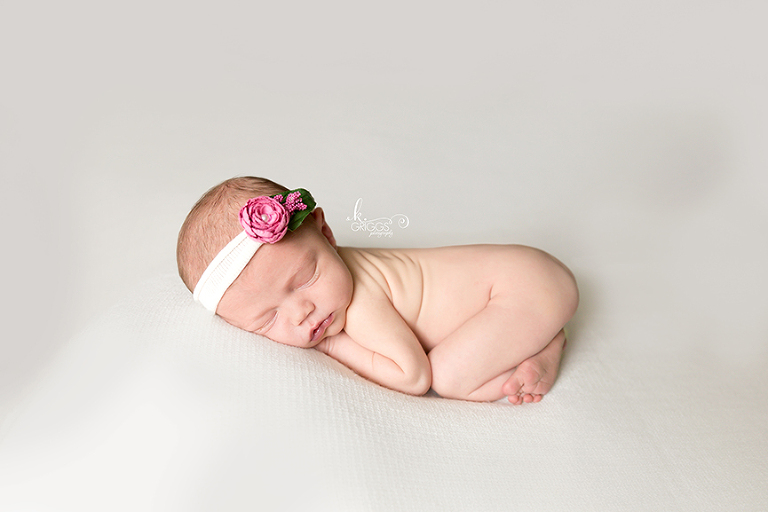 Baby girl curled up asleep on white blanket. | St. Louis Newborn Photos