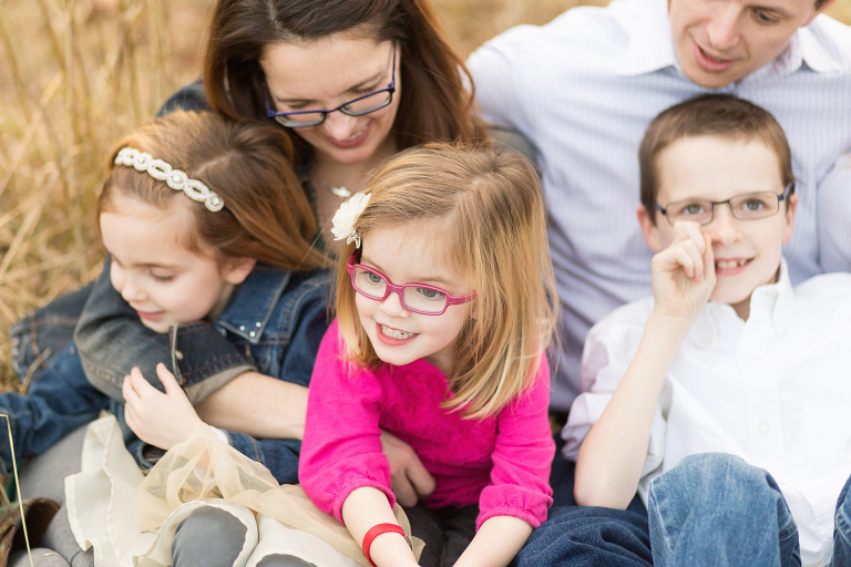 Young girl wearing pink glasses sitting with her family. | Kirkwood Photographer