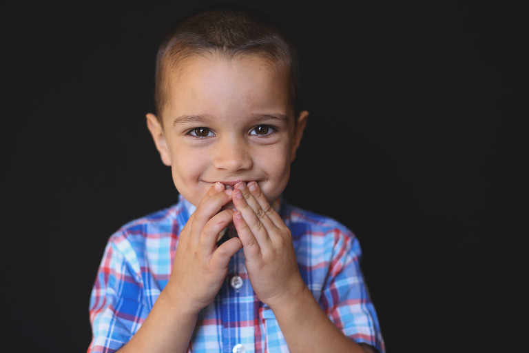 Young boy looking at camera with hands covering mouth | St. Louis School Photographer