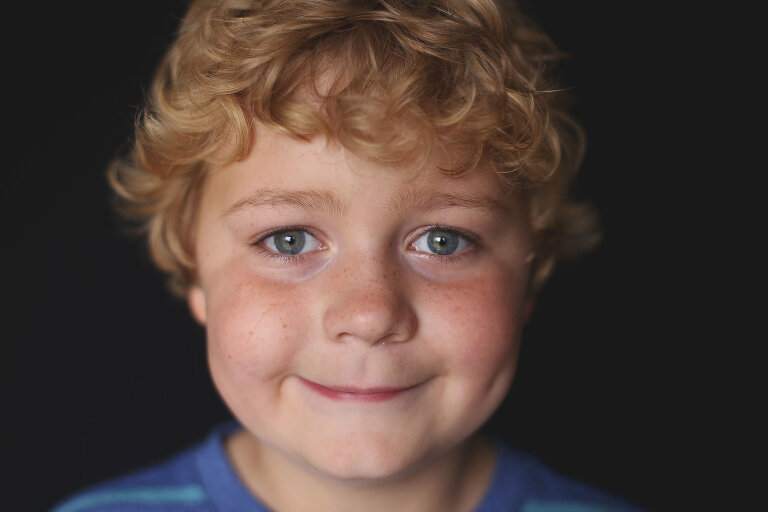 Young boy with curly blonde hair smiling at camera | St. Louis School Photos