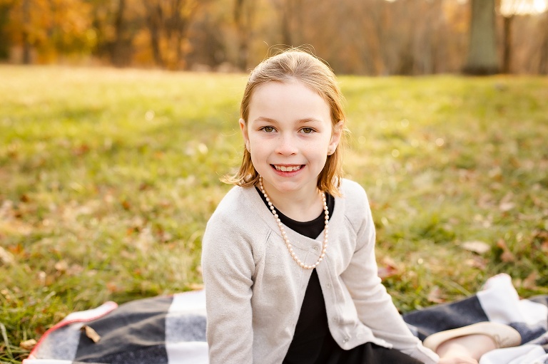 Sweet young girl smiling at camera sitting on blanket | St. Louis Photographer