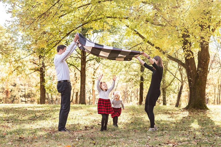 Two girls playing under blanket that is being lifted by parents | STL Family Photography