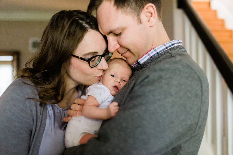 Mom and Dad at in home newborn session kissing their newborn daughter | St. Louis Newborn Photographer